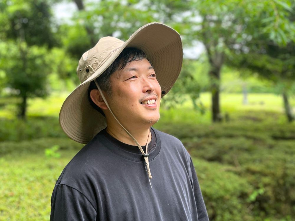植木に囲まれて笑顔の庭師（代表 出山）の写真